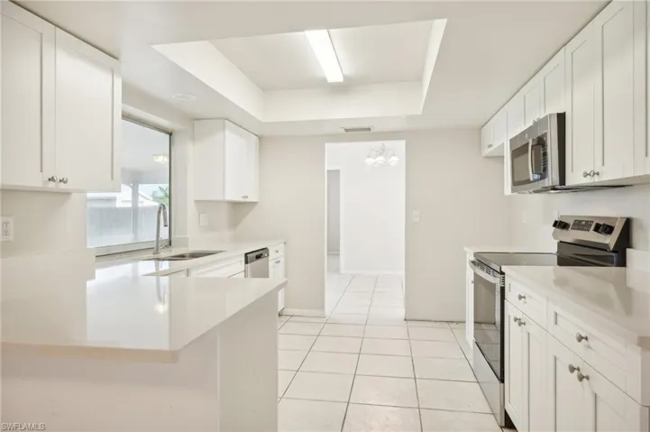 Kitchen with light tile patterned floors, white cabinets, a tray ceiling, appliances with stainless steel finishes, and sink
