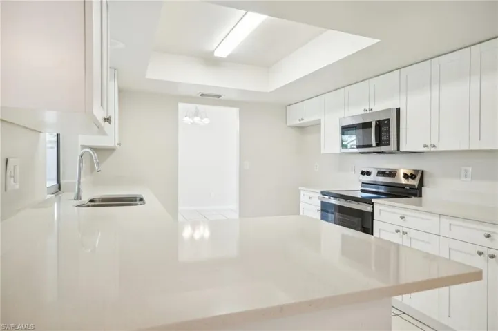 Kitchen with white cabinetry, sink, a raised ceiling, appliances with stainless steel finishes, and kitchen peninsula