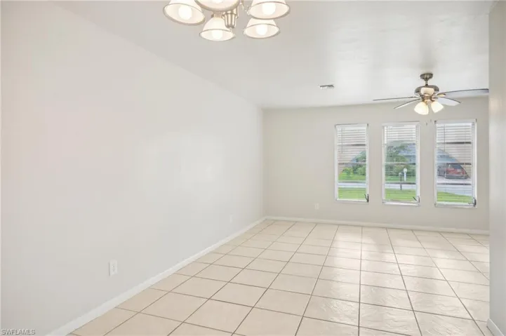 Tiled empty room featuring ceiling fan with notable chandelier