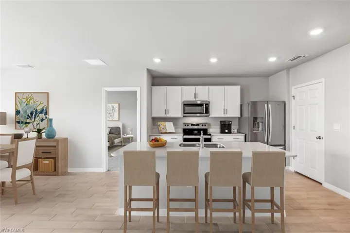 Kitchen with a kitchen island with sink, a breakfast bar area, stainless steel appliances, and white cabinets