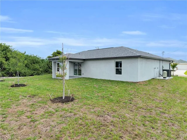 Rear exterior featuring light-colored stucco finish, gray shingle roof, and a covered patio area with sliding glass doors