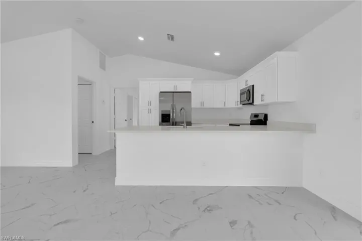 Contemporary kitchen featuring white cabinetry, stainless steel appliances, a breakfast bar, and vaulted ceilings