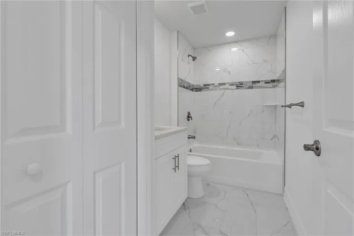 Bathroom featuring a white bathtub, marble-look wall tile with a decorative accent band, and a coordinating marble-look floor tile