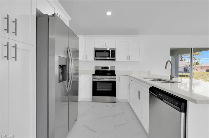 Bright kitchen featuring white shaker cabinetry, stainless steel appliances, light countertops, and large format floor tiling