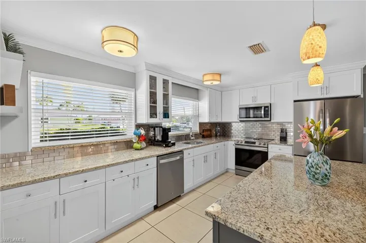 Kitchen with decorative backsplash, appliances with stainless steel finishes, white cabinetry, light tile patterned flooring, and crown molding