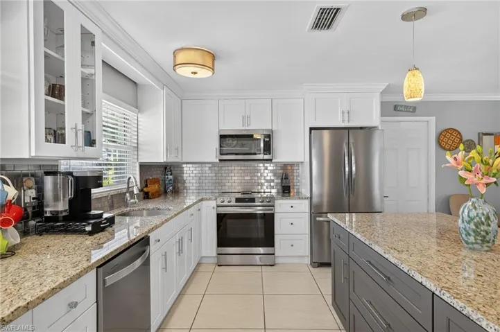 Kitchen with white cabinetry, backsplash, stainless steel appliances, decorative light fixtures, and light tile patterned floors