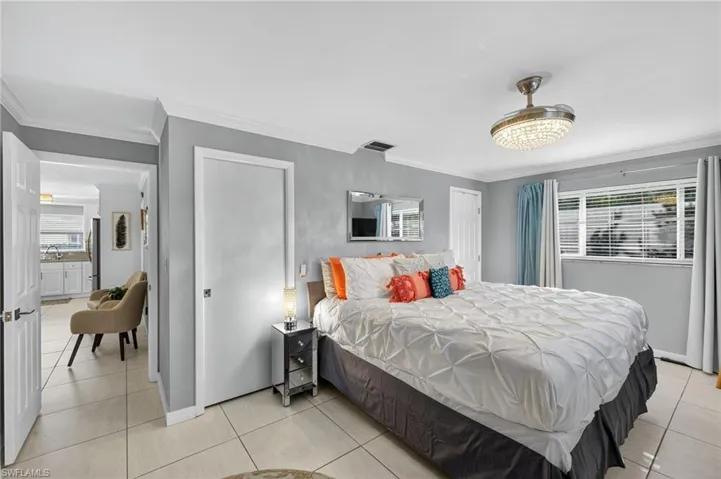 Bedroom with multiple windows, ornamental molding, light tile patterned flooring, and freestanding refrigerator