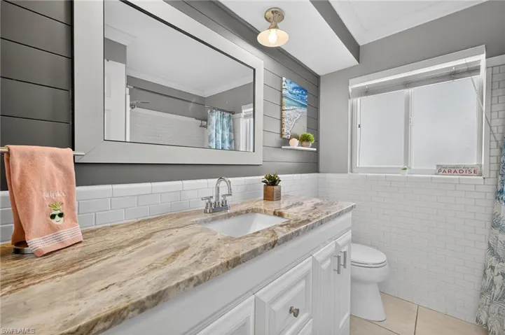 Bathroom featuring vanity, ornamental molding, tile walls, light tile patterned floors, and curtained shower