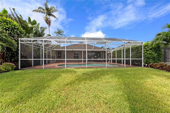 Back of property with a sunroom, a patio, an outdoor pool, glass enclosure, and a yard