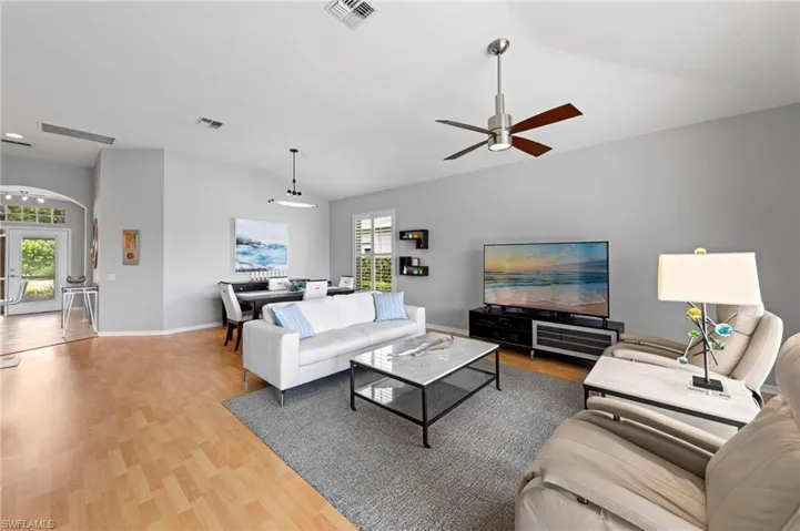Living area with lofted ceiling, arched walkways, light wood finished floors, french doors, and ceiling fan