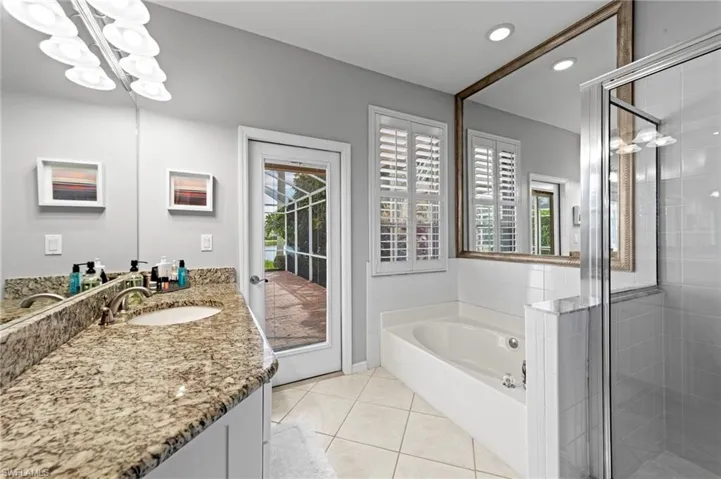 Bathroom featuring a stall shower, vanity, light tile patterned flooring, a garden tub, and a chandelier