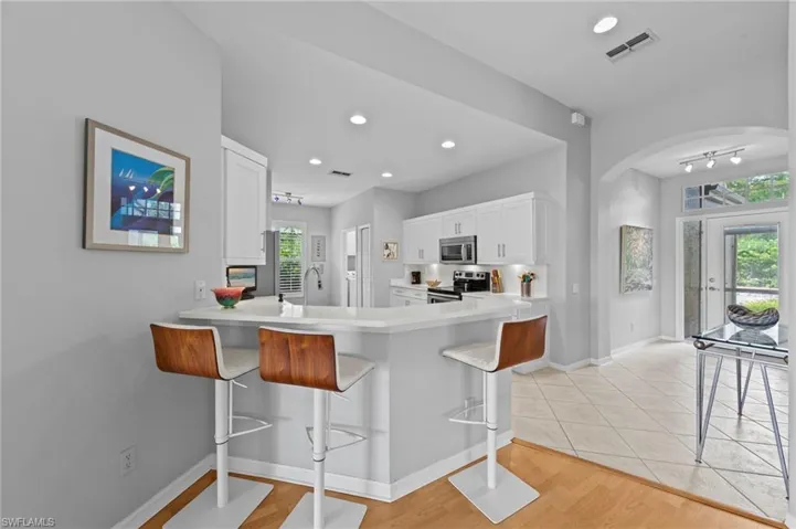 Kitchen with a breakfast bar area, arched walkways, white cabinets, light wood-style floors, and stainless steel appliances