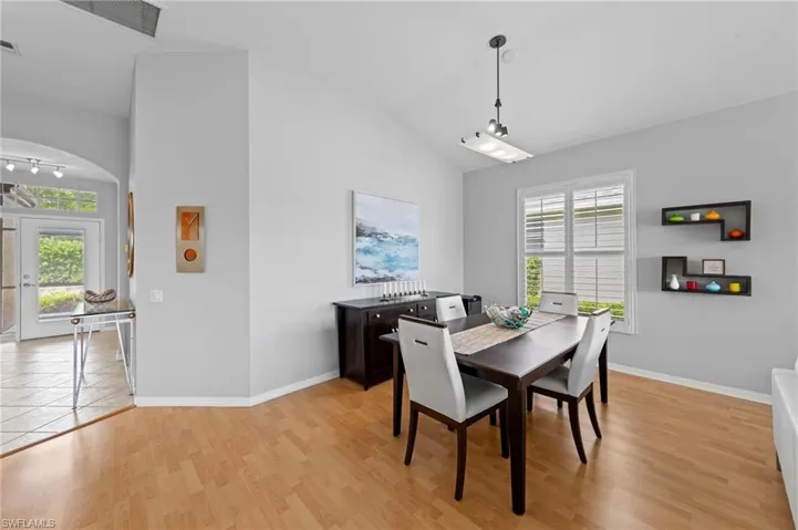 Dining space with lofted ceiling, arched walkways, and light wood-style floors
