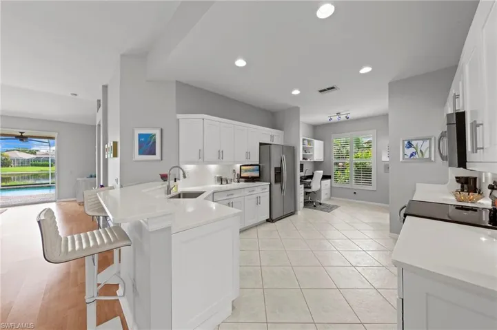 Kitchen with a peninsula, white cabinetry, stainless steel appliances, a kitchen bar, and an office area