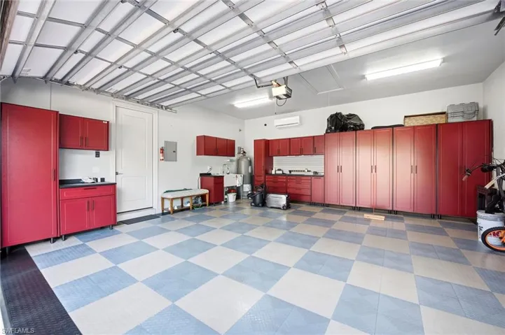 Multi-car garage featuring checkerboard flooring, extensive red built-in cabinetry, dual overhead fluorescent lighting, and a wall-mounted climate control unit