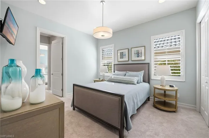 Neutral-toned interior space featuring light-colored wall-to-wall carpeting, dual windows fitted with plantation shutters, a modern drum-style pendant light fixture, and multi-panel interior doors