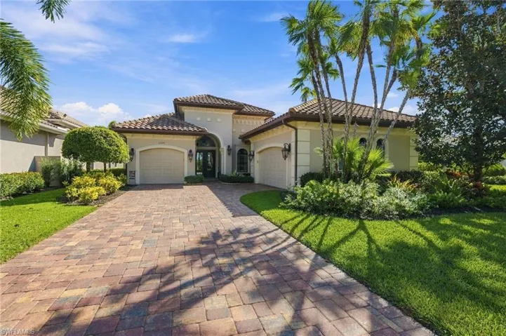 Mediterranean-style exterior featuring a tile roof, stucco facade, paver driveway, three-car garage, and established landscaping