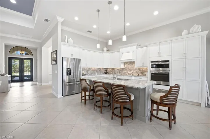 Kitchen featuring white cabinetry, stone-finish countertops, stainless steel appliances, a central island with a built-in sink, and pendant lighting