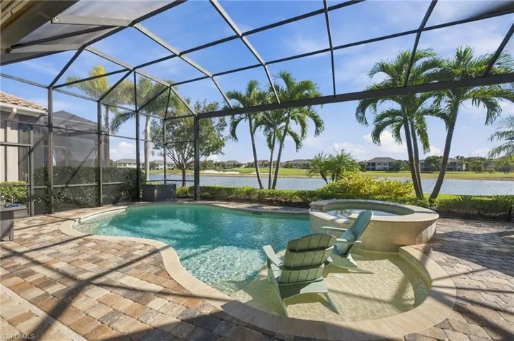 Screen-enclosed patio featuring a paver deck, custom pool, integrated spa, and Baja shelf