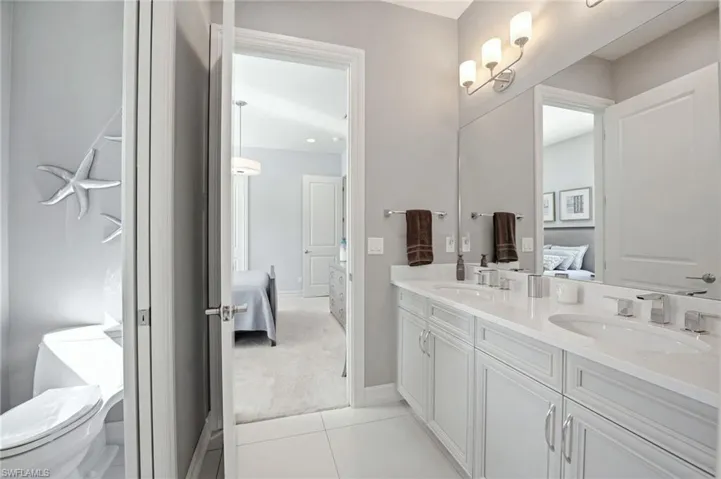 Dual-sink vanity with white cabinetry and light-toned countertop, undermount sinks, polished chrome fixtures, full-width vanity mirror, and multi-bulb wall lighting