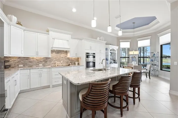 Kitchen featuring white cabinetry, stone-tiled backsplash, large center island with stone countertop, built-in double oven, and tray ceiling with recessed lighting