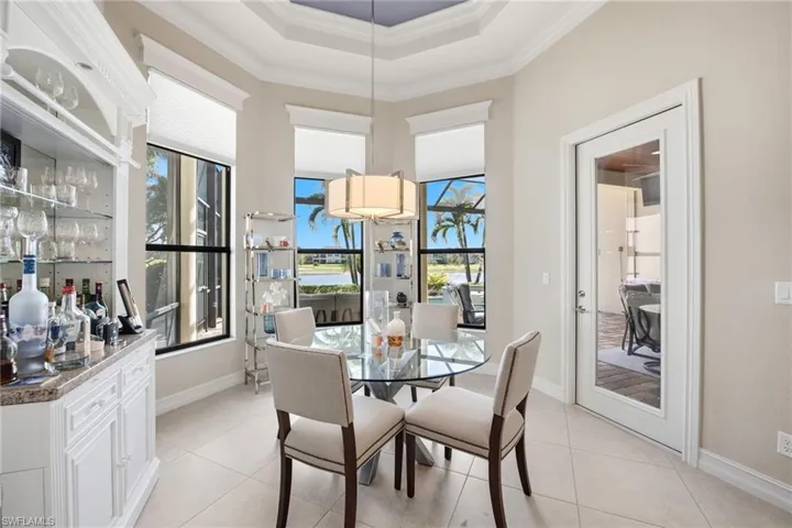 Tray ceiling with recessed lighting, built-in cabinetry featuring integrated glass shelving, expansive windows with custom casing, neutral tile flooring, and a glass-paneled entry door