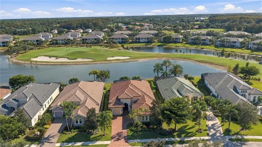 Aerial perspective featuring residential lots with tile roofing, paver driveways, and established palm landscaping, situated along a central water feature with golf course frontage