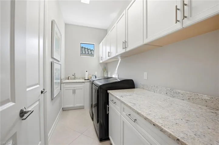 Utility room featuring white cabinetry, stone-finish countertops, tile flooring, an undermount sink with a gooseneck faucet, and extensive upper and lower storage