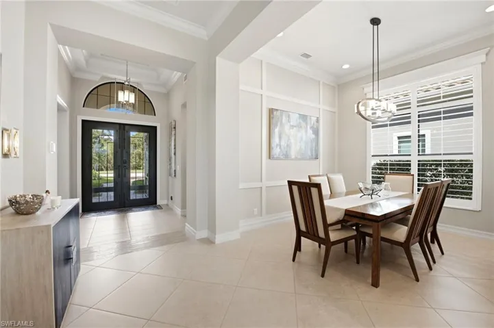 Double front entry doors with a decorative transom window, recessed ceiling detail, tile flooring, grid-pattern wall molding, and a suspended multi-light fixture