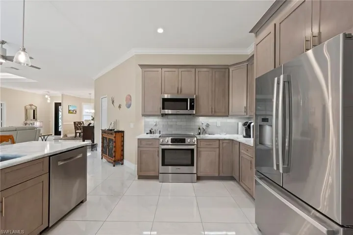 Kitchen featuring light tile patterned flooring, appliances with stainless steel finishes, tasteful backsplash, crown molding, and pendant lighting