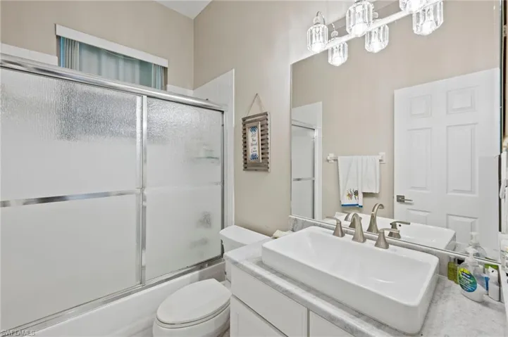 Full bathroom featuring combined bath / shower with glass door, vanity, and toilet