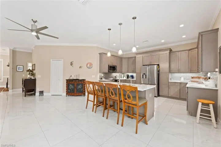 Kitchen with a breakfast bar, stainless steel appliances, a kitchen island with sink, ceiling fan, and crown molding
