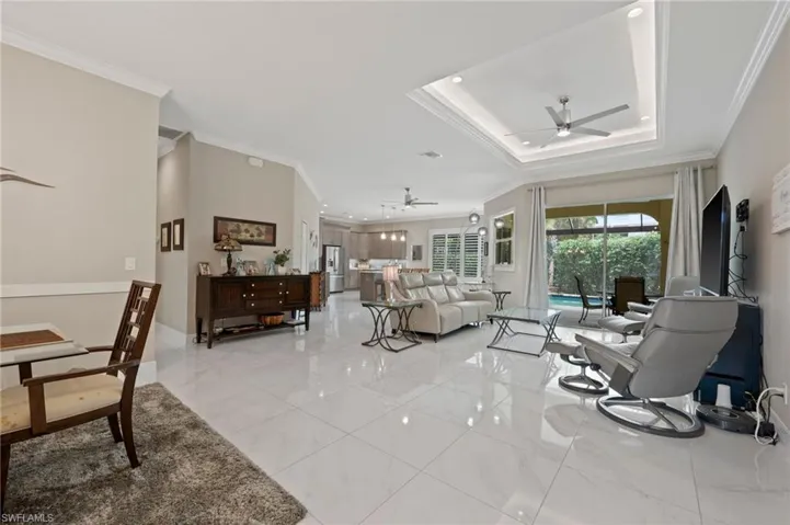 Living room with light tile patterned flooring, ceiling fan, and a raised ceiling