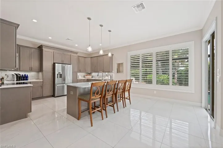 Kitchen featuring a kitchen breakfast bar, an island with sink, light tile patterned floors, decorative light fixtures, and stainless steel fridge