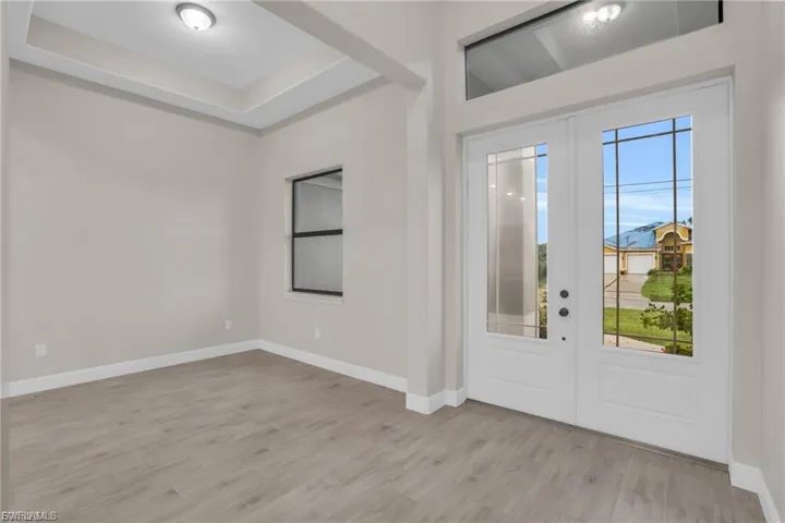 Foyer entrance with light wood-type flooring, french doors, and a tray ceiling