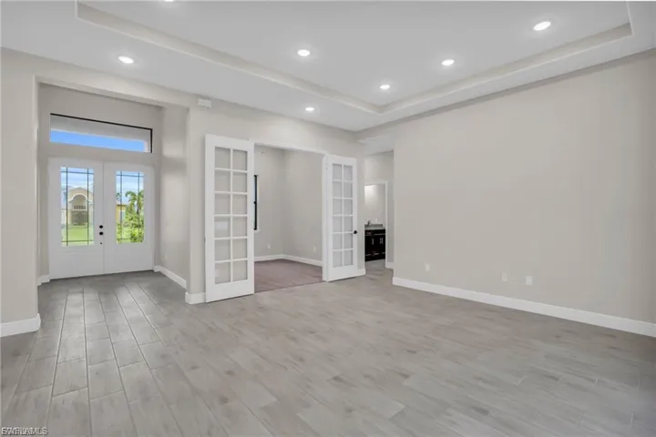 Unfurnished room with french doors, a raised ceiling, light wood-style floors, and recessed lighting