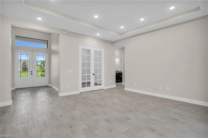 Empty room featuring french doors, a raised ceiling, light wood-style flooring, and recessed lighting