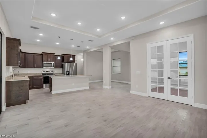 Kitchen featuring hanging light fixtures, a kitchen island, dark brown cabinets, stainless steel appliances, and open floor plan