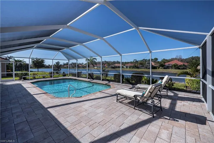 View of pool featuring glass enclosure, a patio area, and a water view