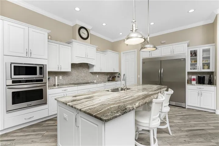 Kitchen with light stone countertops, built in appliances, a kitchen breakfast bar, white cabinets, and tasteful backsplash