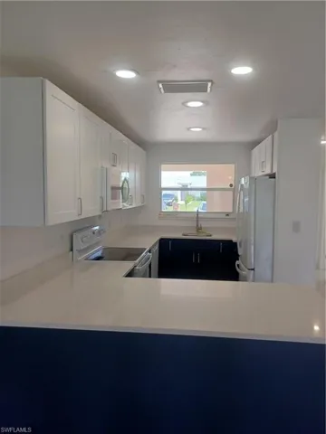 Kitchen with stove, fridge, recessed lighting, white cabinets, and a peninsula