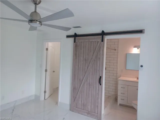 Unfurnished bedroom featuring a barn door, light marble finish flooring, and connected bathroom