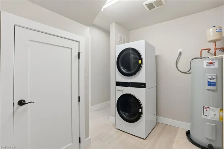 Laundry area with electric water heater, stacked washer and dryer, and light wood-type flooring - Virtually Edited Image