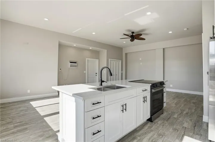 Kitchen with electric range, light wood finished floors, a ceiling fan, light stone countertops, and recessed lighting - Virtually Edited Image