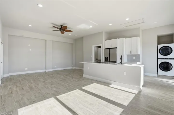 Kitchen featuring light wood-type flooring, white cabinetry, an island with sink, a ceiling fan, and stainless steel fridge with ice dispenser - Virtually Edited Image