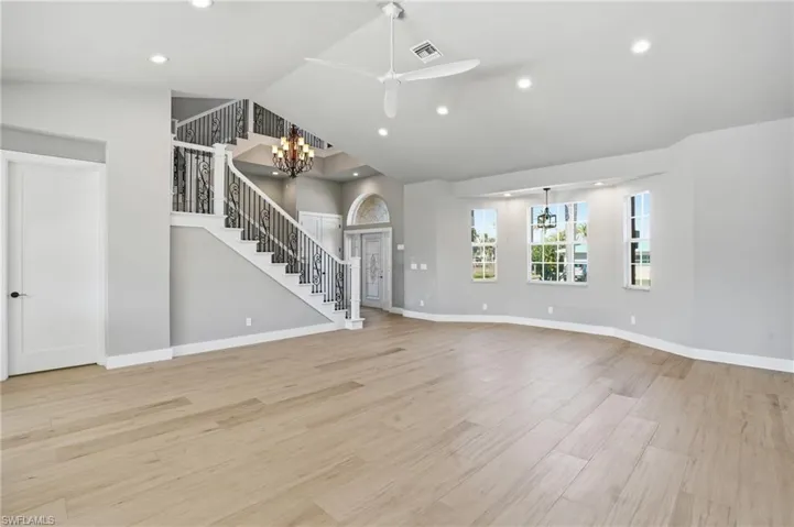 Unfurnished living room with hanging lights, ceiling fan, light wood-style flooring, and vaulted ceiling - Virtually Edited Image