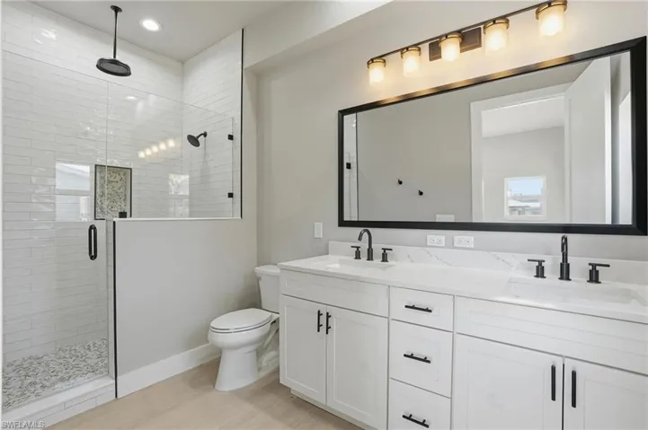 Bathroom featuring a stall shower, double vanity, and light wood-type flooring - Virtually Edited Image