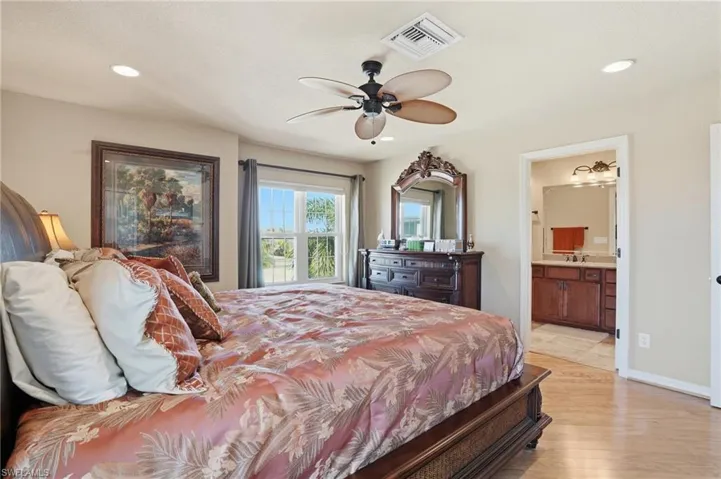 Bedroom featuring light wood-style flooring, ceiling fan, connected bathroom, and recessed lighting - Virtually Edited Image