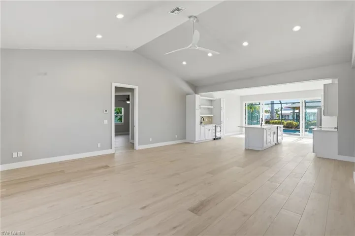Unfurnished living room featuring ceiling fan, recessed lighting, light wood-type flooring, wine cooler, and a high ceiling - Virtually Edited Image