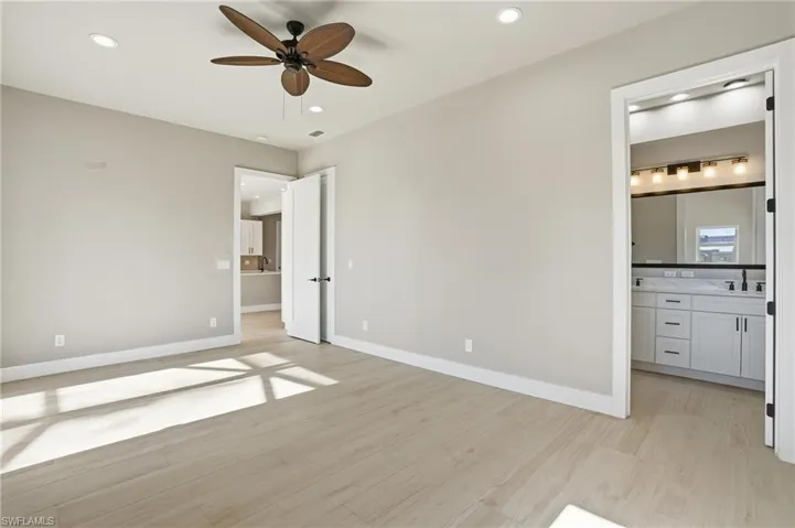 Unfurnished bedroom with ensuite bath, light wood finished floors, ceiling fan, and recessed lighting - Virtually Edited Image